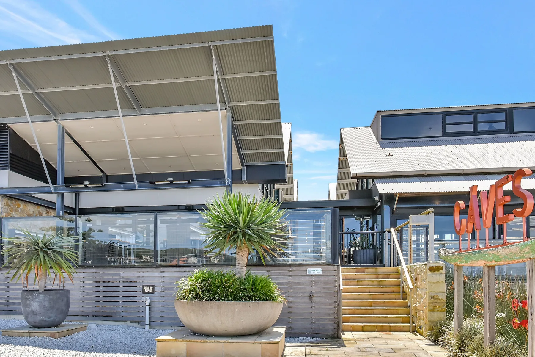 A modern building exterior with broad roof canopies, glass windows, and potted plants.