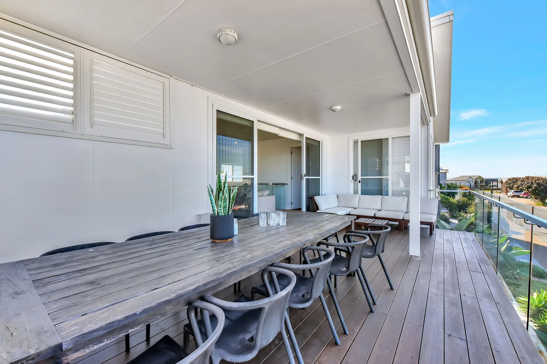 A covered outdoor dining area with a long table and seating beside glass doors.
