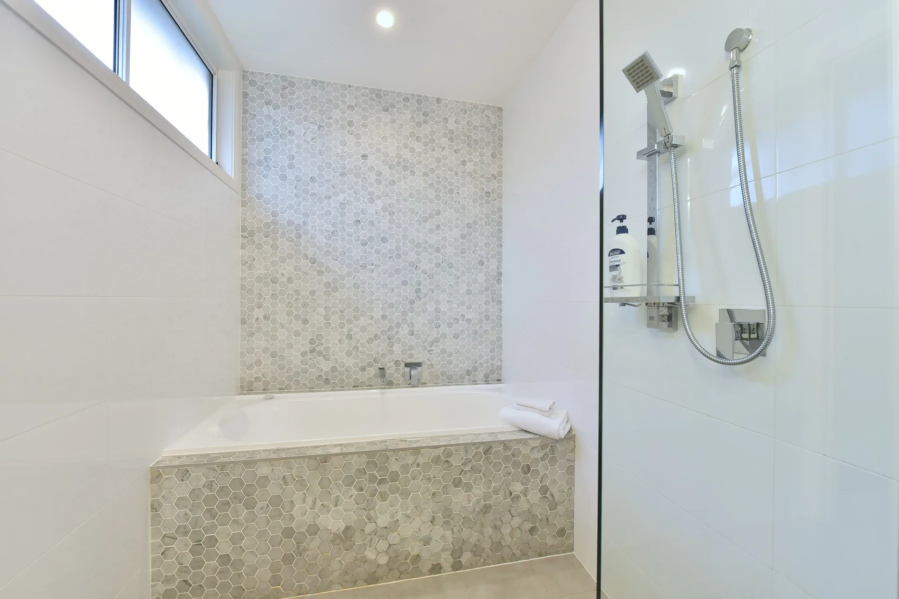 A bright bathroom features a tiled bathtub beside a glass-enclosed shower.