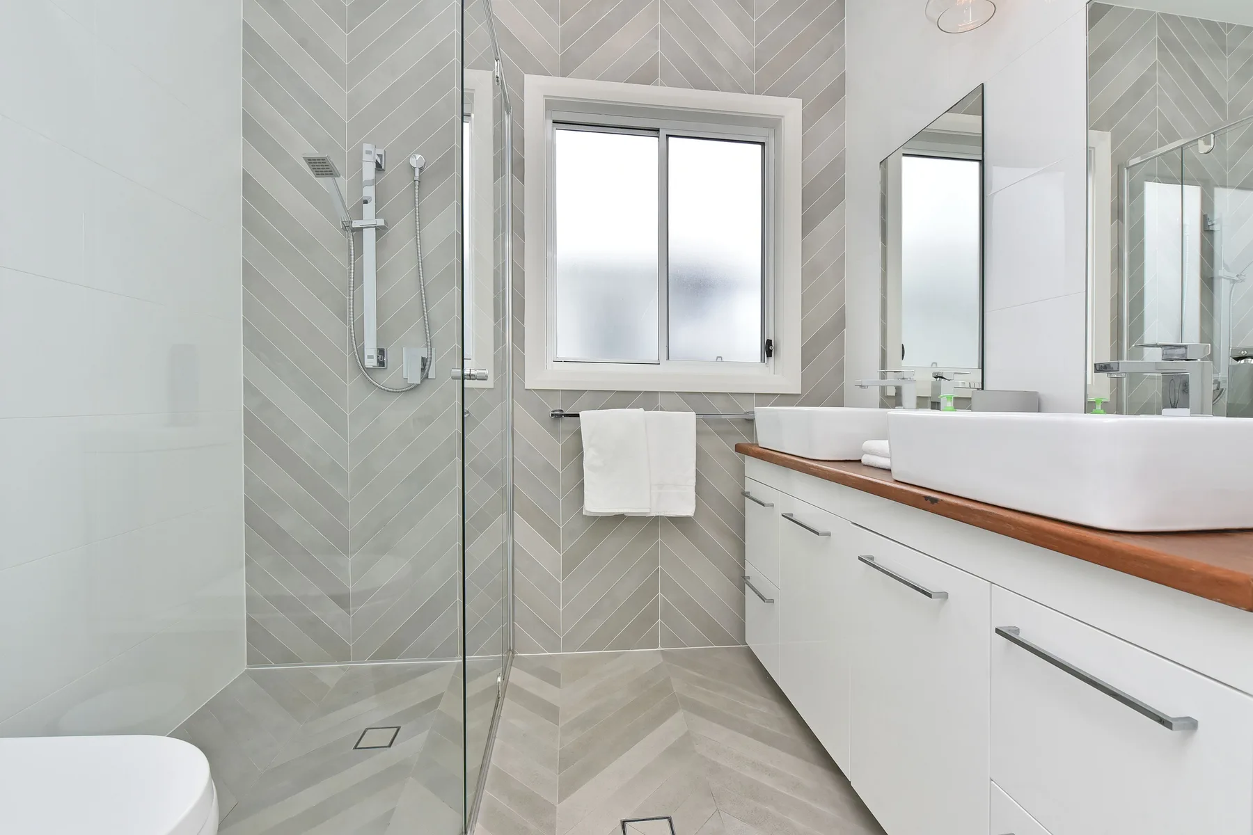 A modern bathroom with a glass shower, window, and vanity.