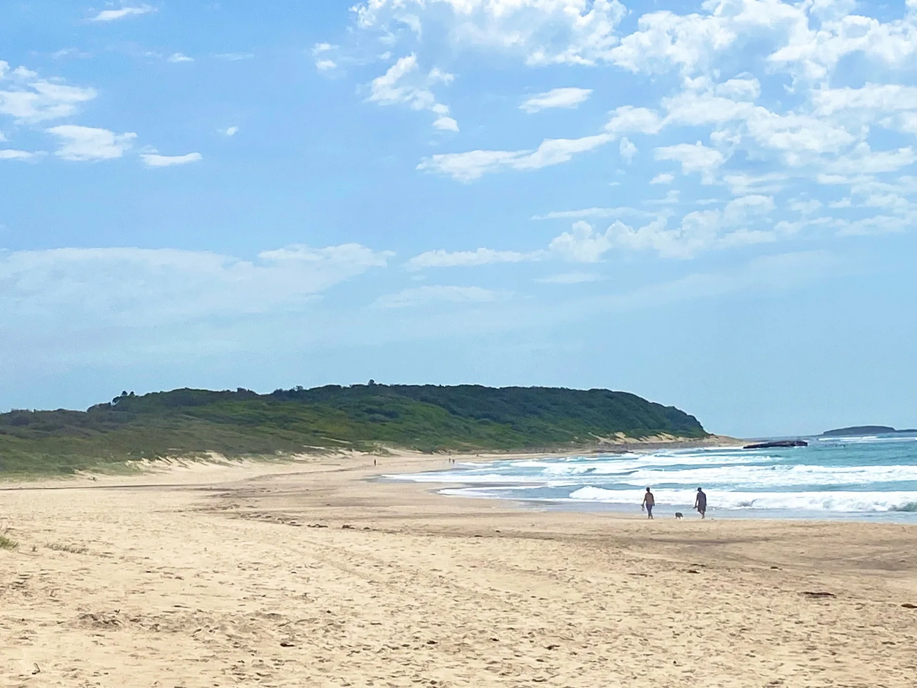 A sandy beach curves along the shoreline beneath a partly cloudy sky.