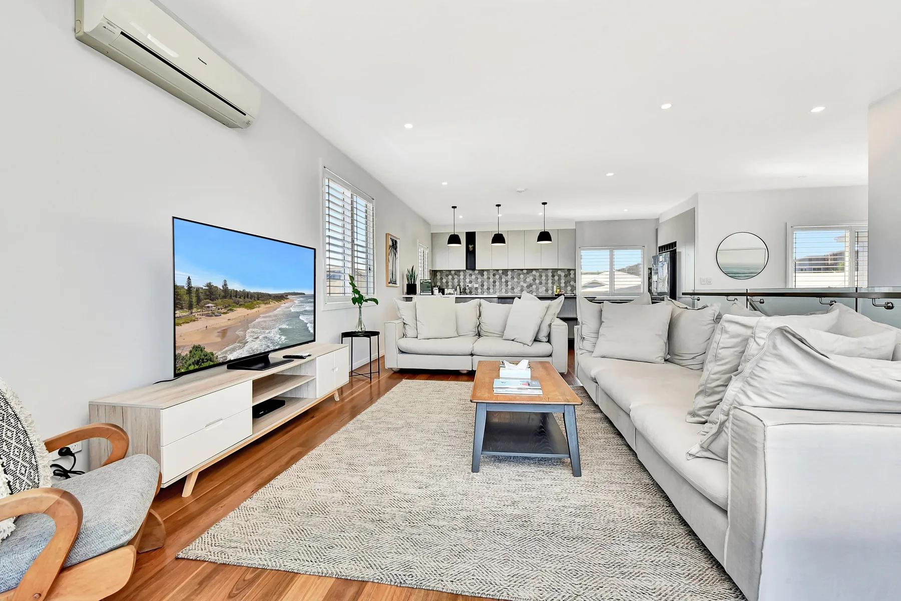 A bright living room with white seating, a television, and an open kitchen.
