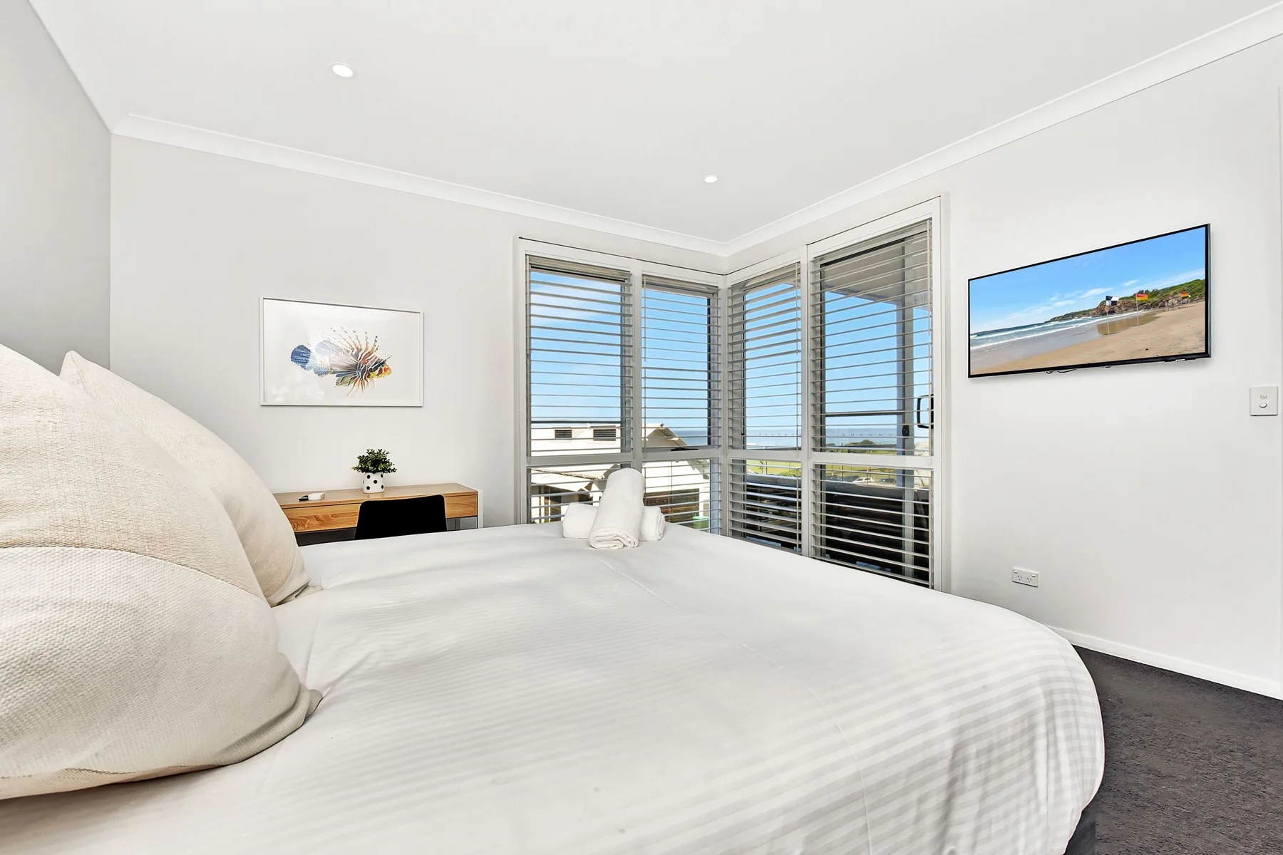 A bright bedroom with a neatly made bed and windows overlooking the beach.