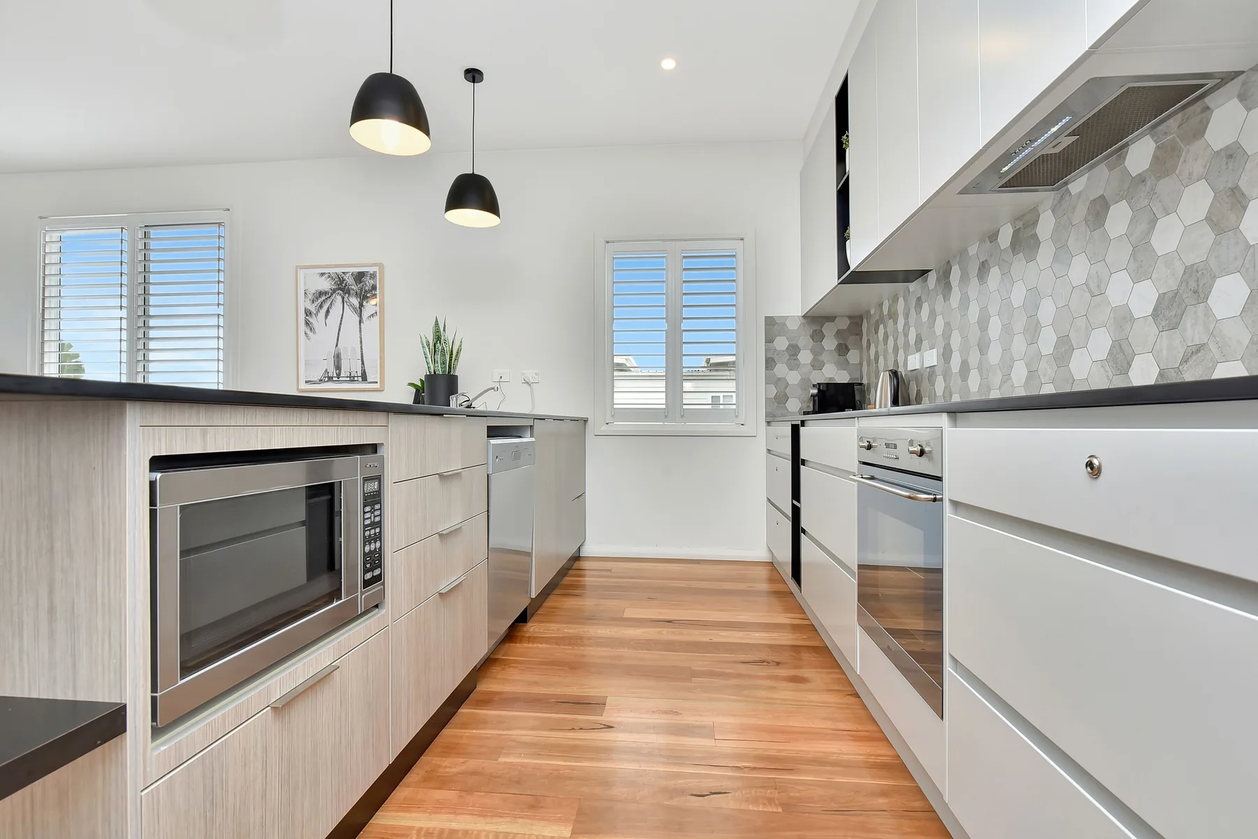 A modern kitchen with light cabinetry and wood flooring.