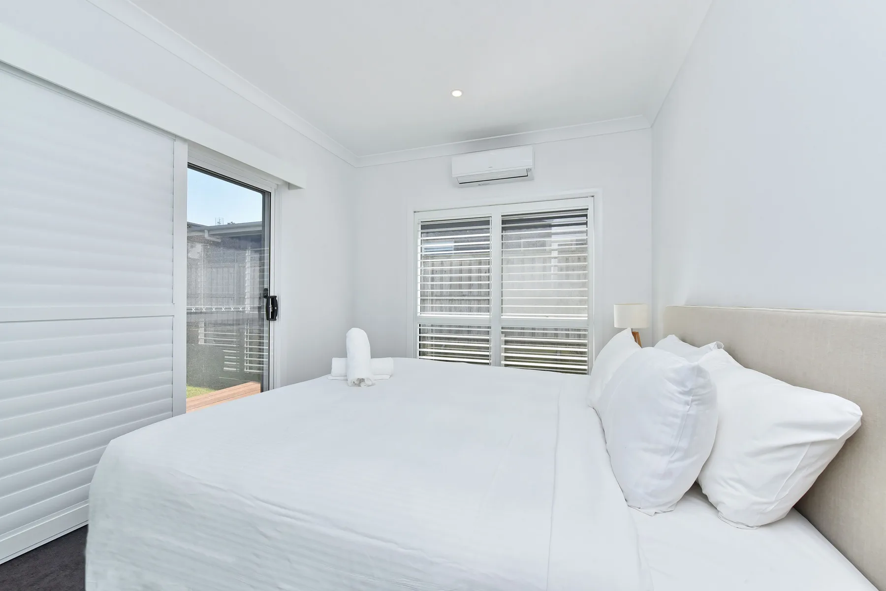 A bright bedroom with a bed beside a window and sliding glass door.