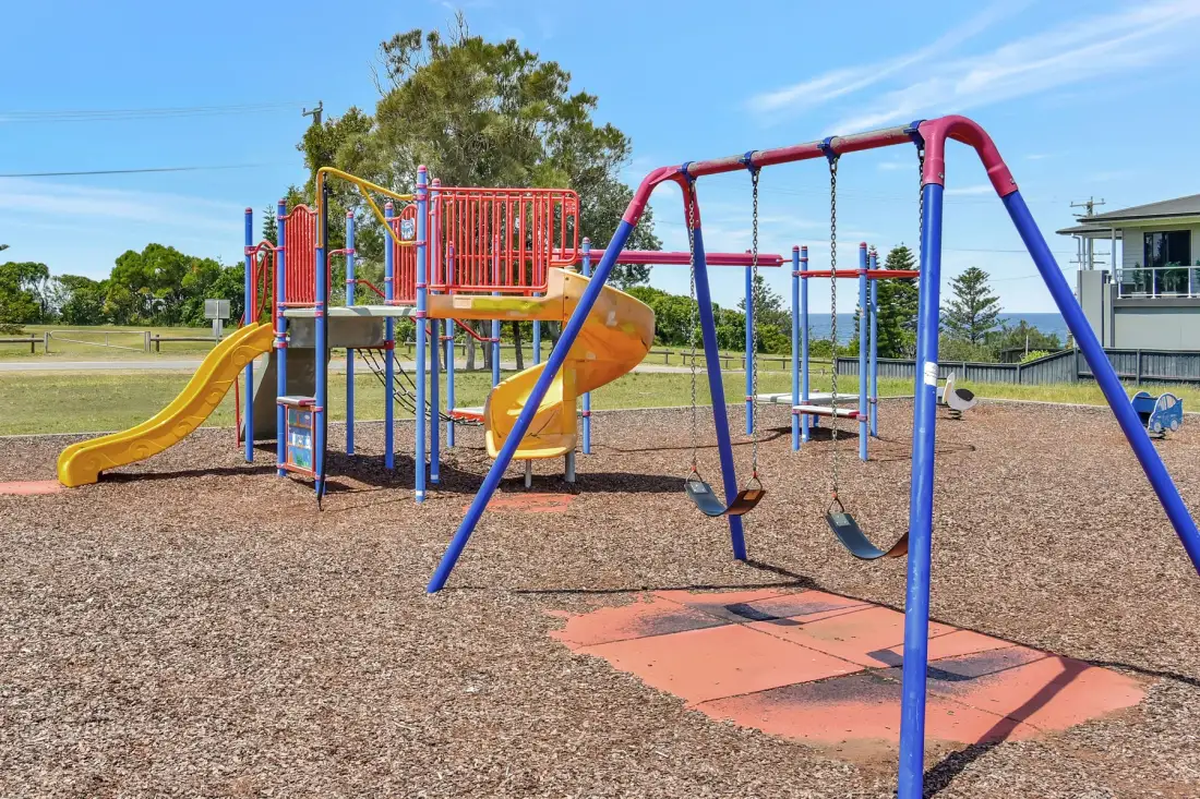 A colorful playground with slides and swings stands on a gravel surface.