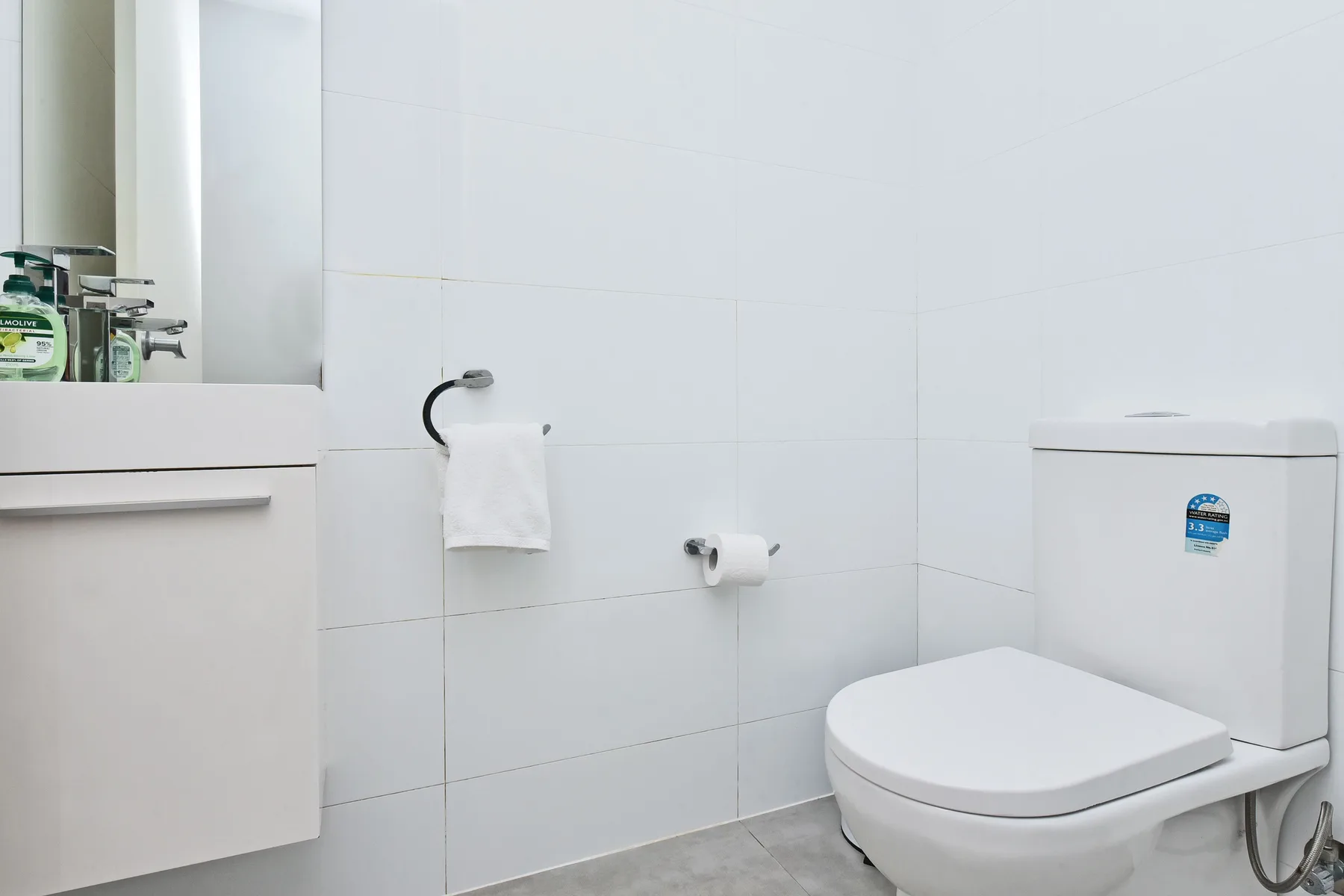 A bathroom with a toilet, wall-mounted toilet paper holder, and towel rail.