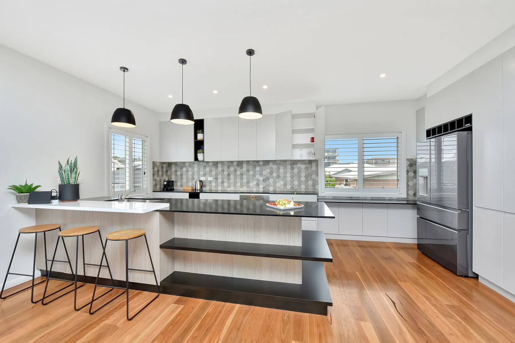 A bright modern kitchen with a long island, pendant lights, and wood flooring.