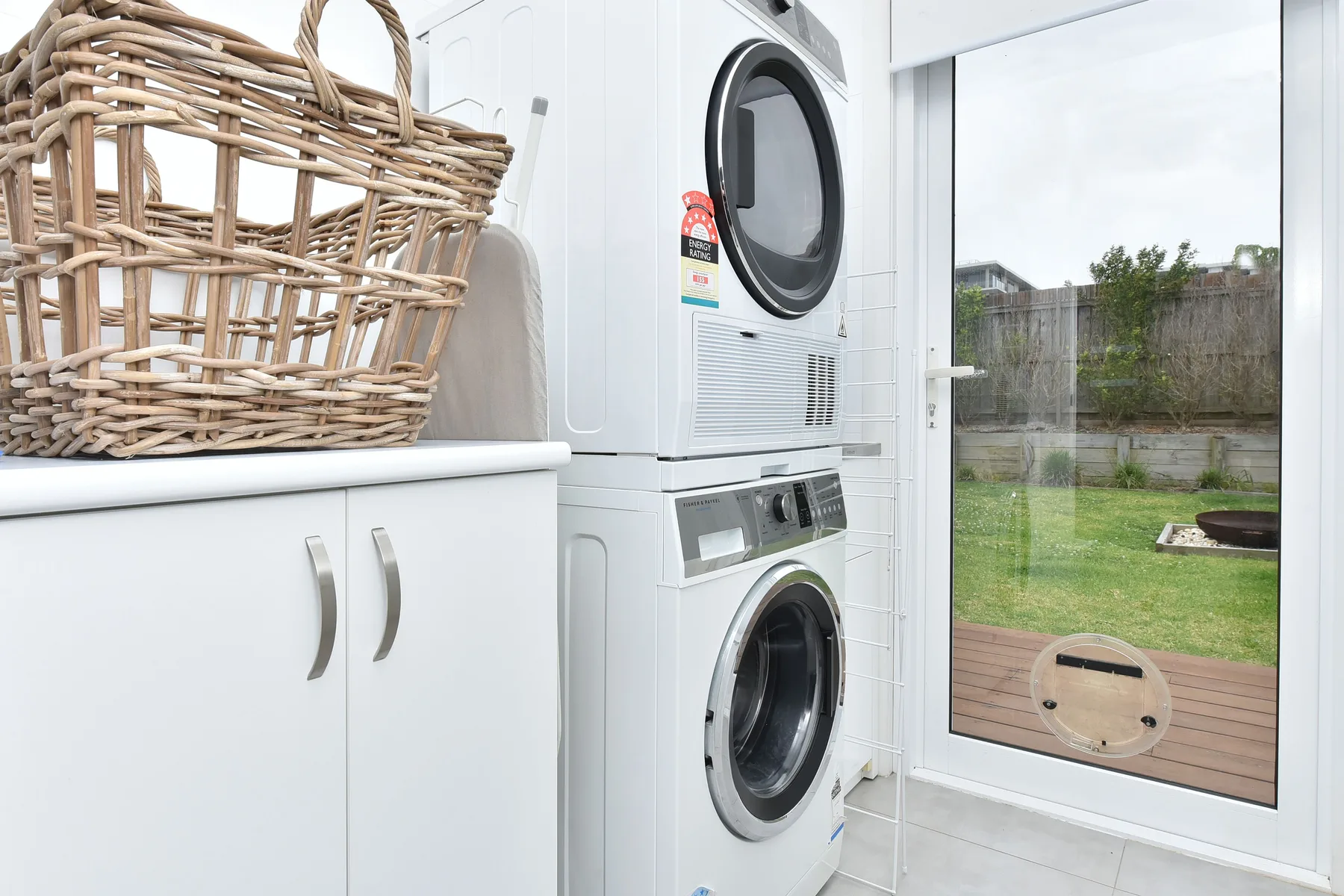 A laundry area with stacked washing machines beside a glass door overlooking a yard.