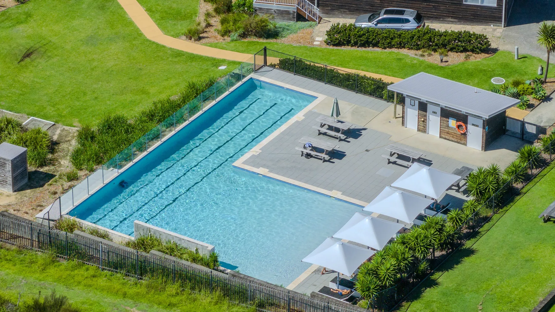 An outdoor swimming pool with lounge chairs, umbrellas, and a small pool building.