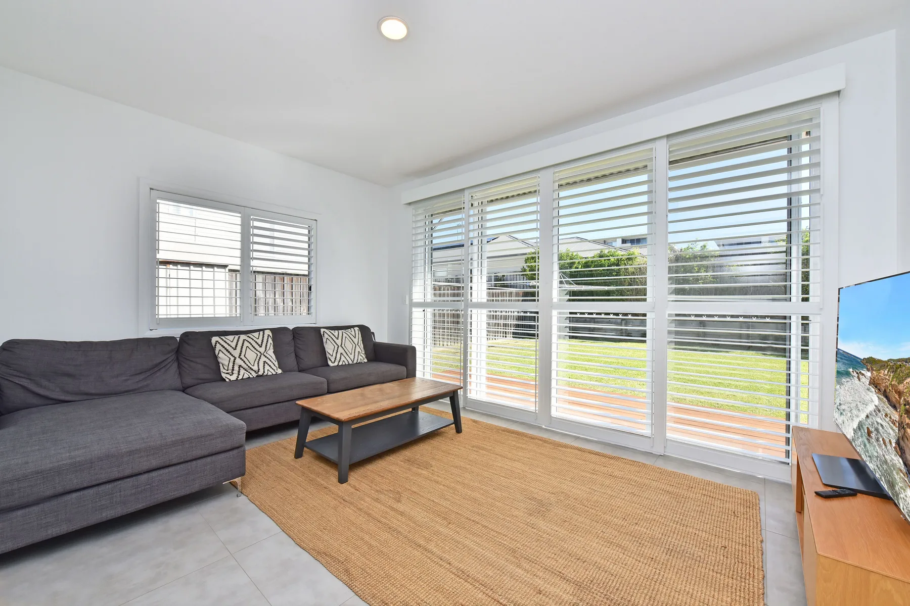 A bright living room with a dark sectional sofa and wide windows overlooking a lawn.