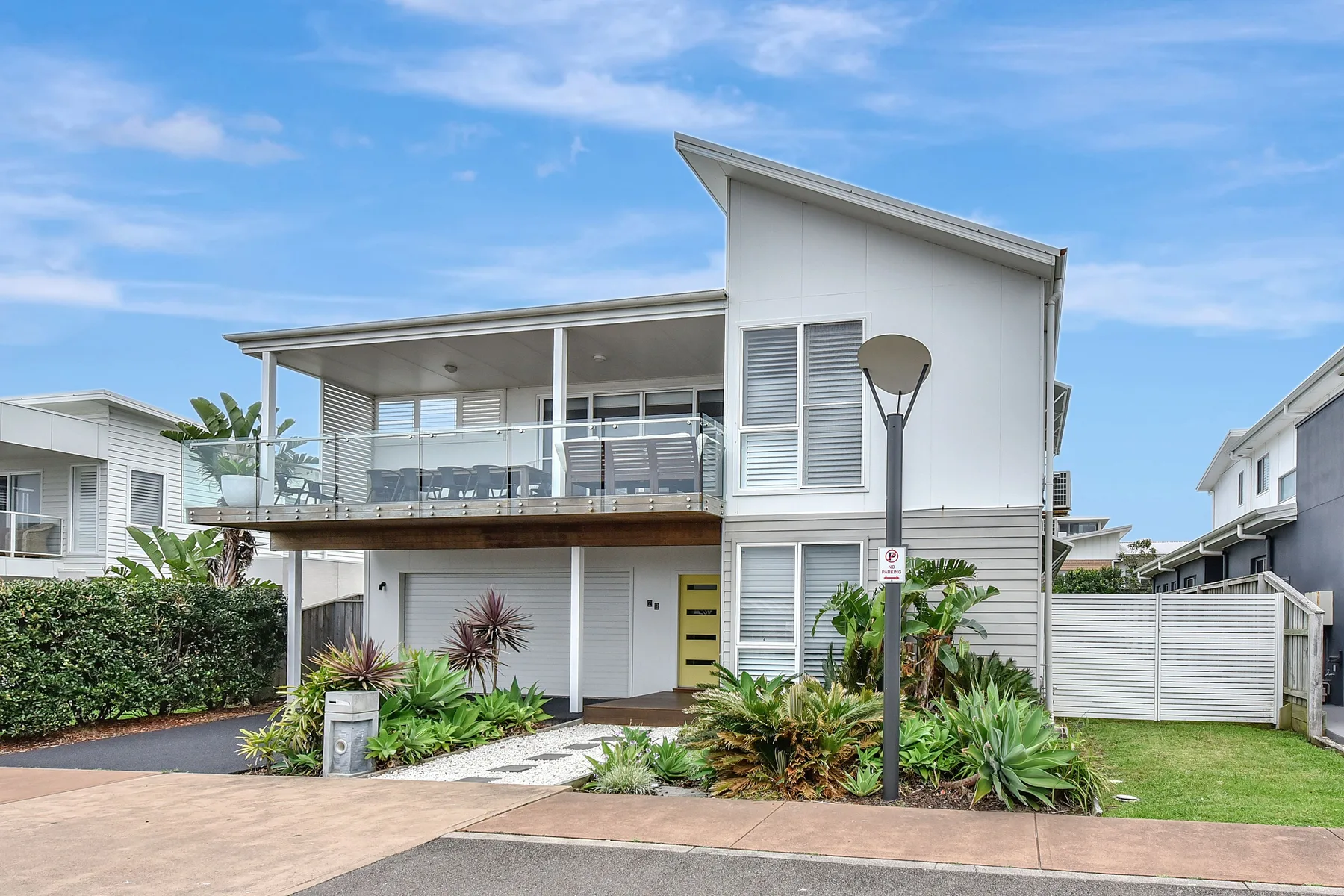 A modern coastal house with an upper balcony and landscaped garden.