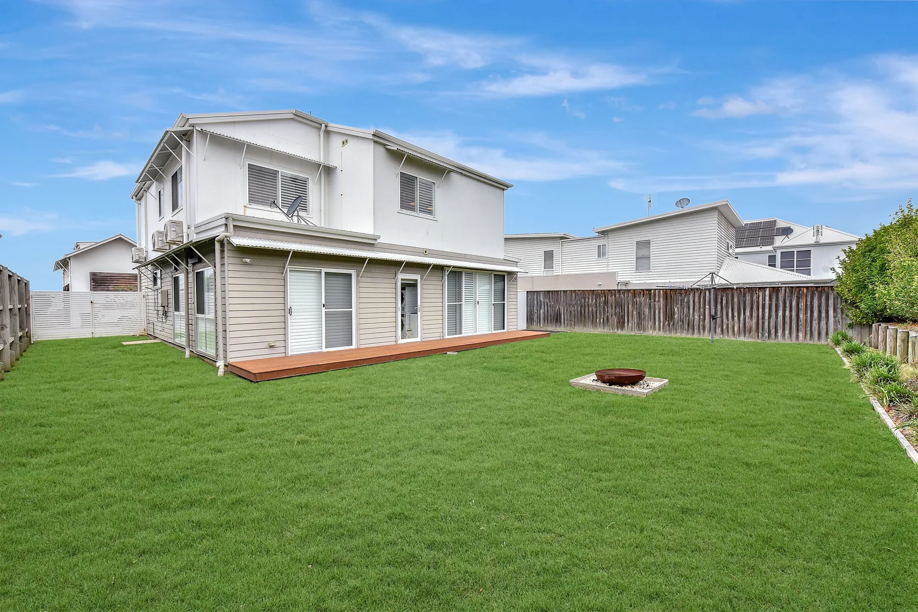 A two-story house with a deck stands beside a broad green lawn.
