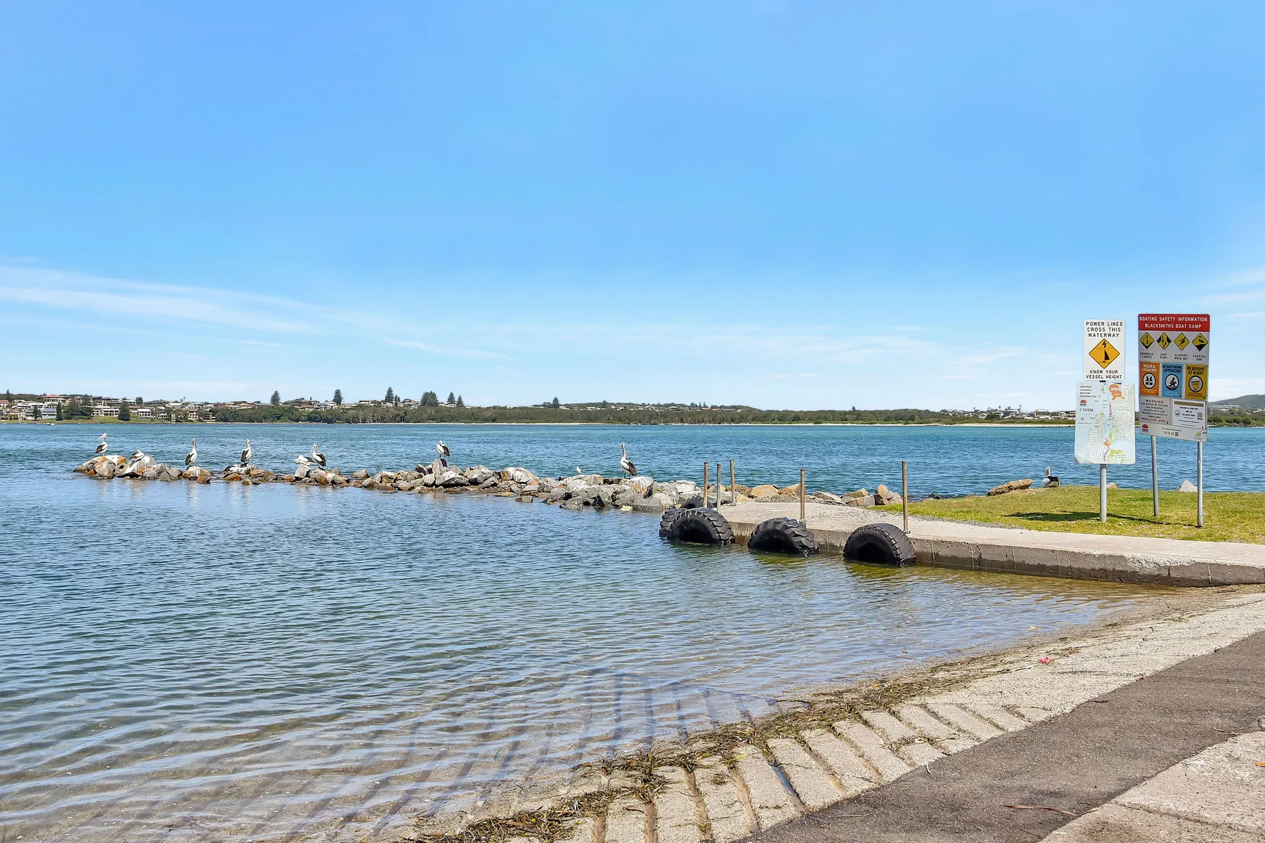 A waterfront launch ramp extends into calm water beneath a clear sky.