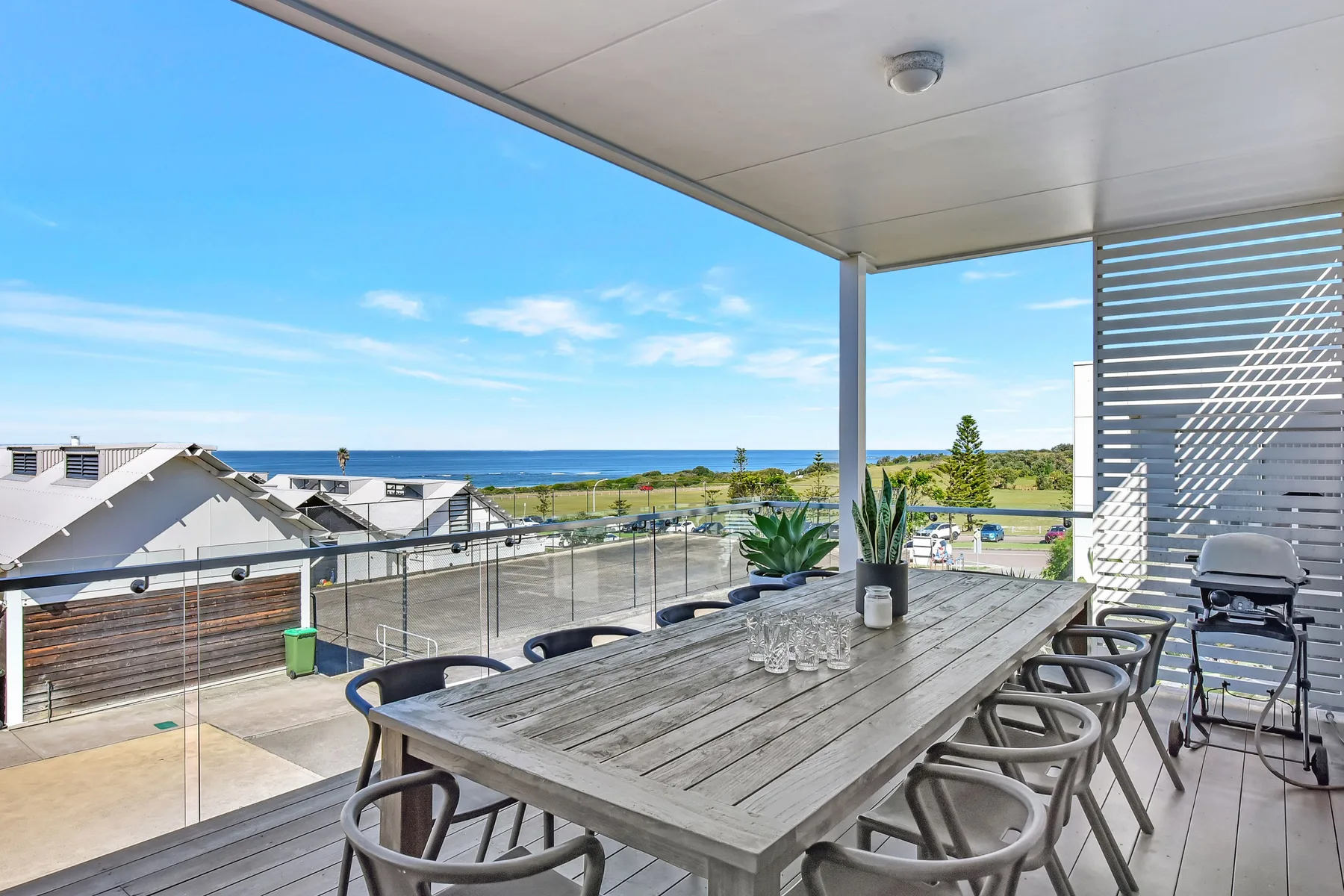 A covered outdoor dining area with a long table overlooks the ocean.
