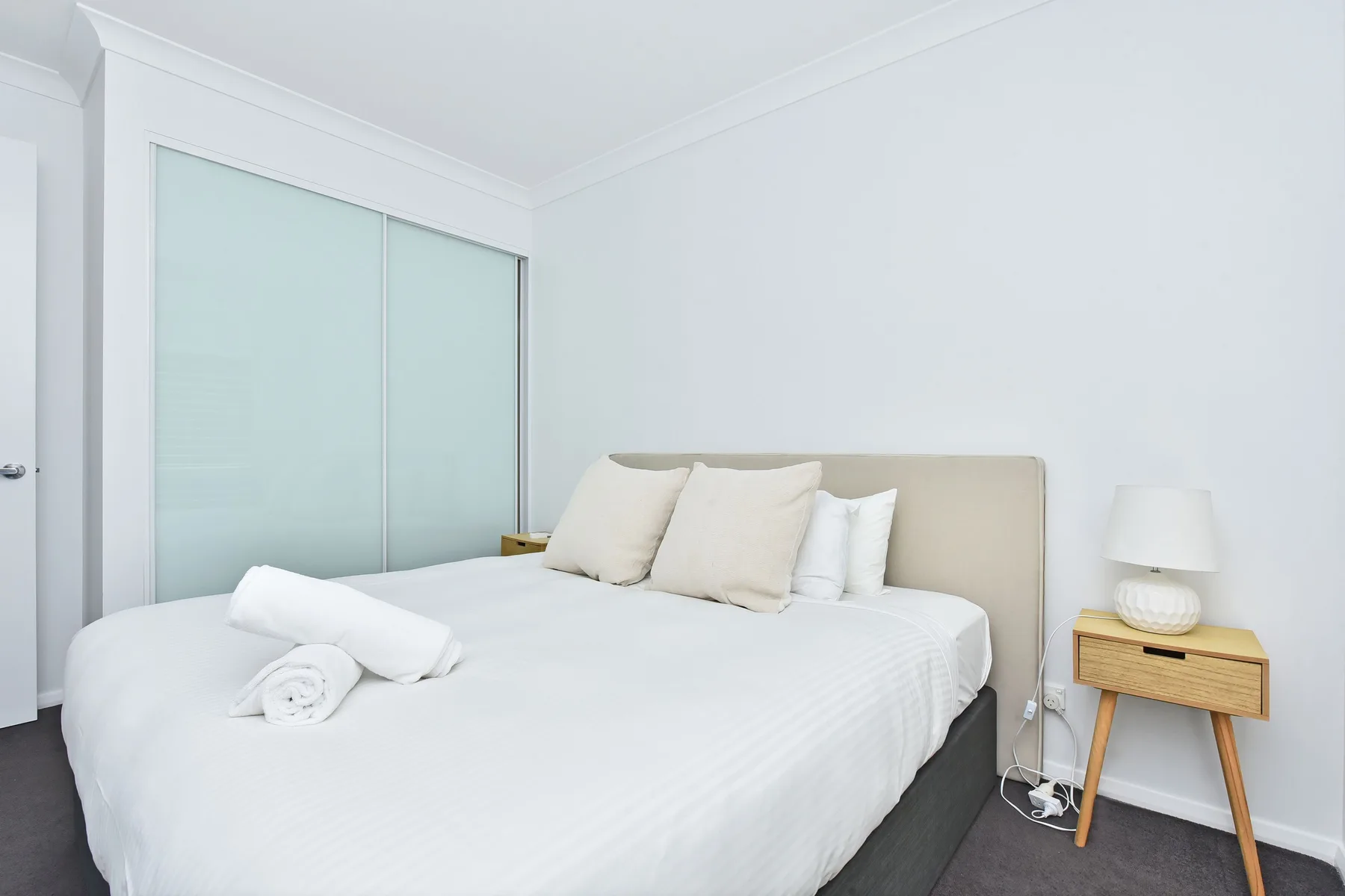 A bright bedroom with a neatly made bed and bedside table.