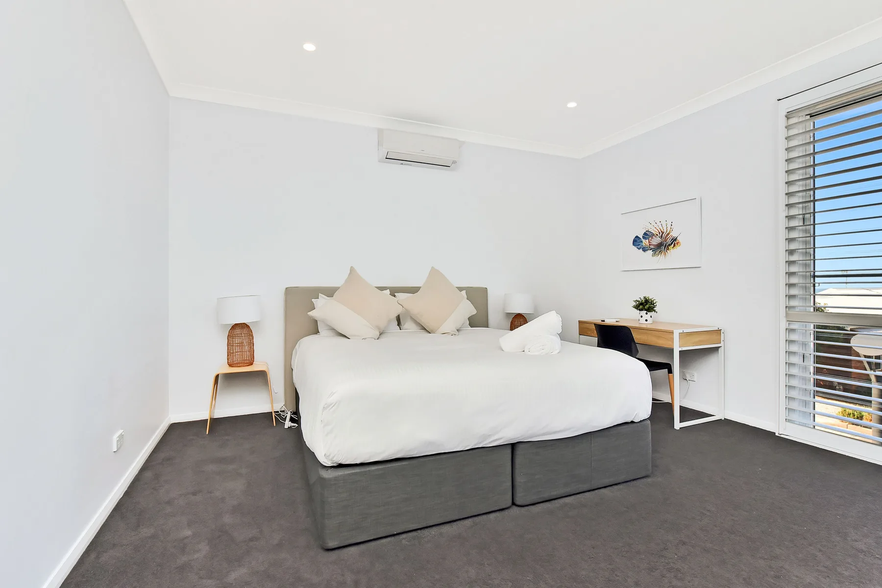 A bright bedroom with a neatly made bed and a desk beside the window.