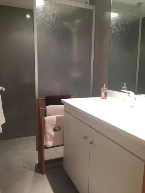 Baño con lavabo blanco, ducha con mampara de cristal y toallero.