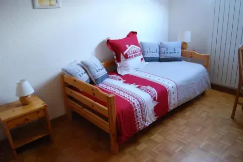 Habitación con ropa de cama roja y blanca y mesita de noche de madera.