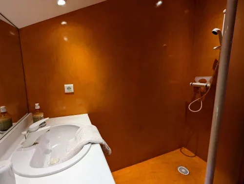 Baño con paredes de color óxido, lavabo blanco y ducha a ras de suelo.