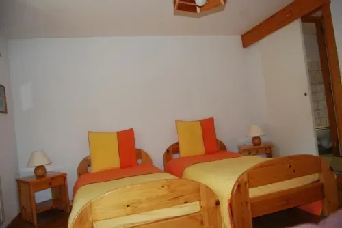 Habitación luminosa con dos camas de madera y ropa de cama roja y amarilla.