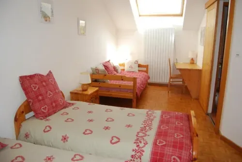 Habitación abuhardillada con camas de madera, ropa de cama roja estampada, tragaluz y suelo de parquet.