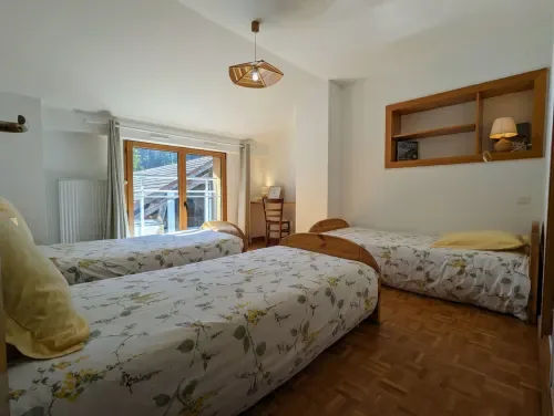 Habitación con tres camas individuales, vigas de madera y balcón con vistas al jardín.