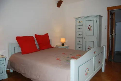 Habitación con cama blanca, cojines rojos y ropa de cama floral.