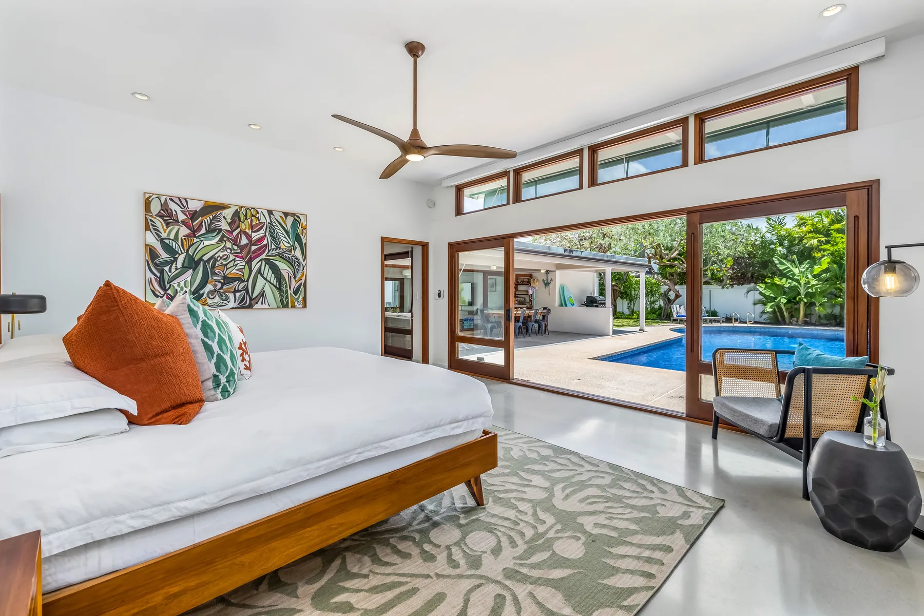 A bright bedroom opens onto a patio and swimming pool through wide sliding doors.