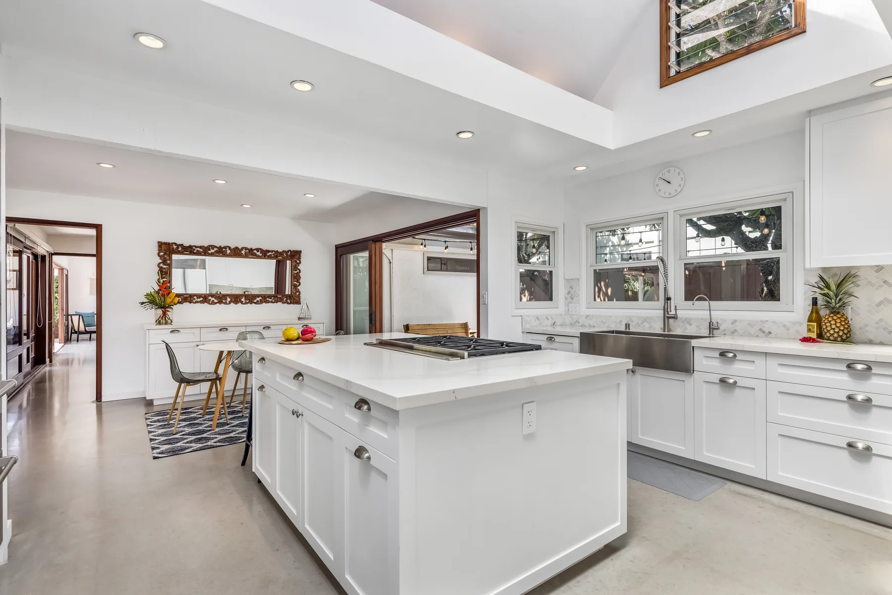 Una cocina blanca y luminosa con isla central, comedor y ventanas.