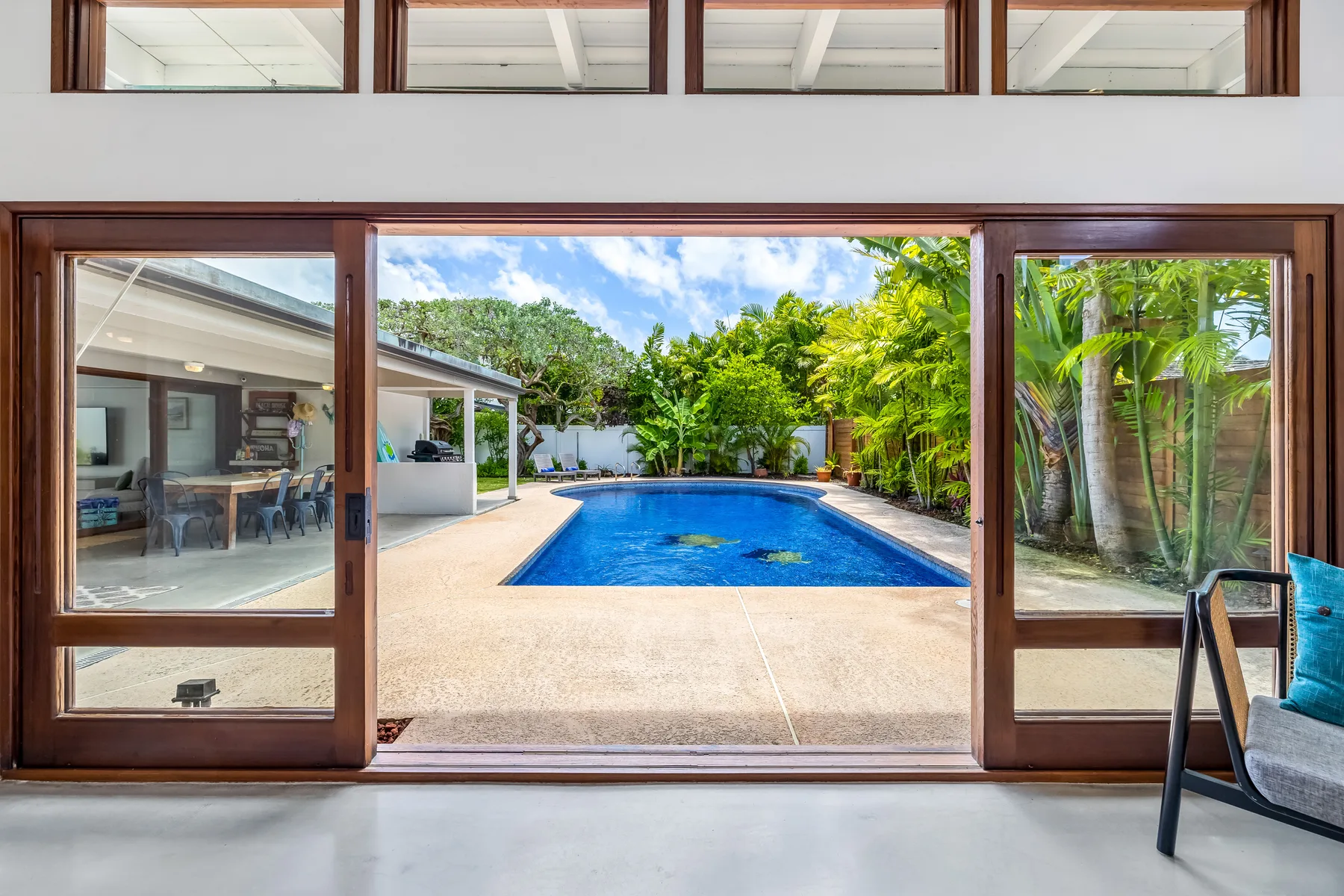 Se ven una piscina y un jardín frondoso a través de amplias puertas corredizas de vidrio.