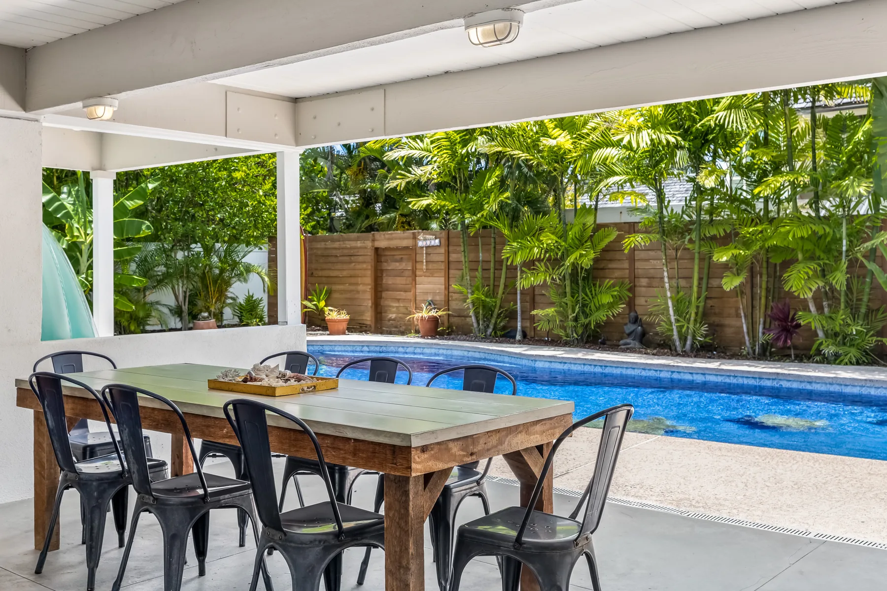 Una zona de comedor cubierta da a una piscina y un jardín frondoso.