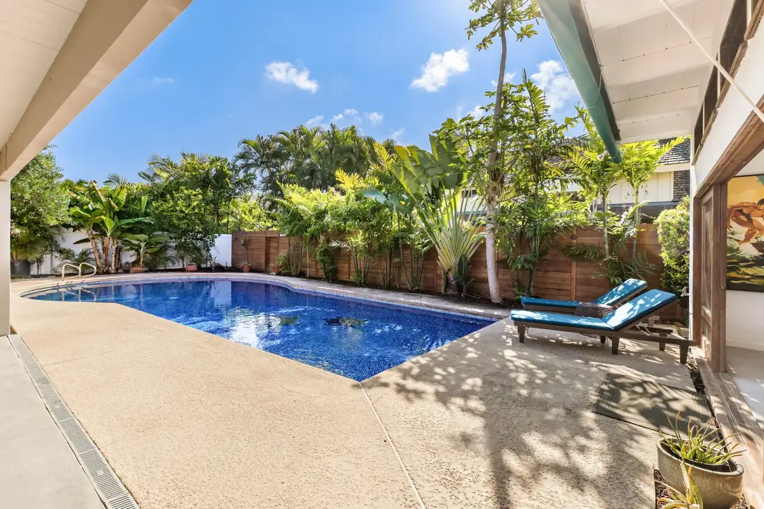 Una piscina al aire libre está rodeada de vegetación y una zona pavimentada para descansar.