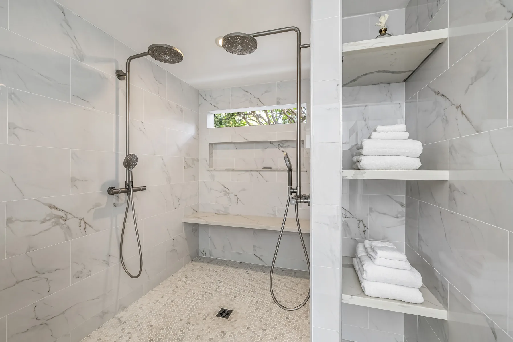 Una zona de ducha con azulejos, rociadores de lluvia y estantes con toallas dobladas.