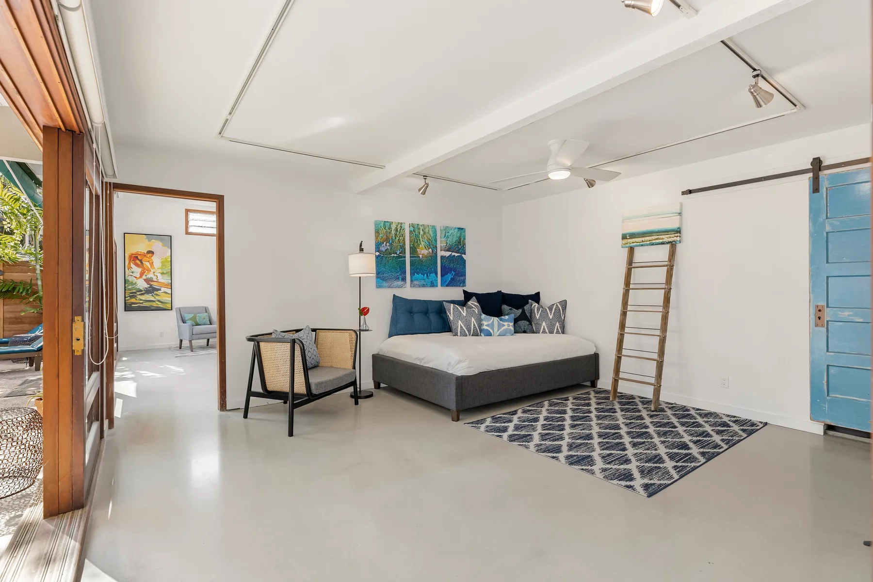 Un dormitorio luminoso tiene una cama, una alfombra estampada y ventanas grandes.