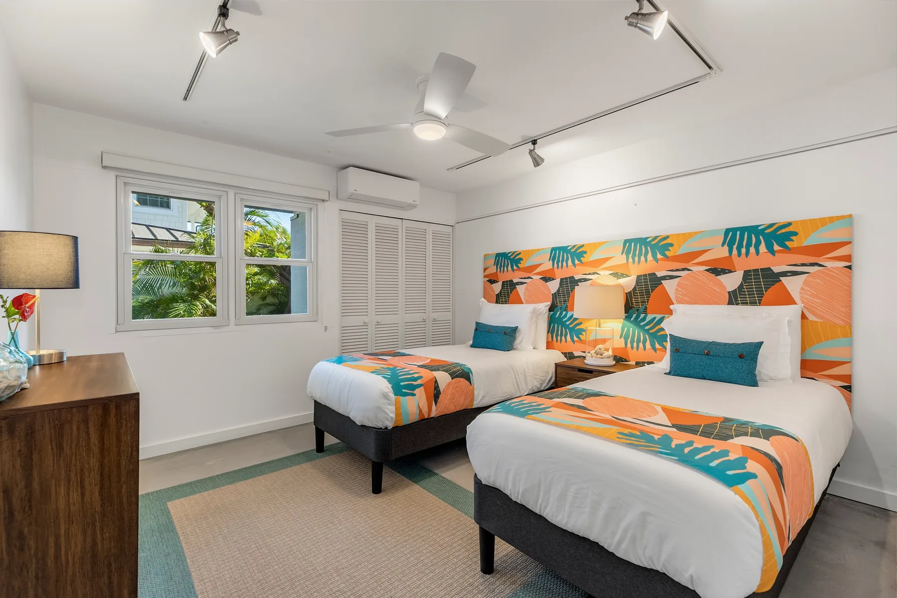 Un dormitorio luminoso con dos camas vestidas con ropa de cama de estampado tropical colorido.
