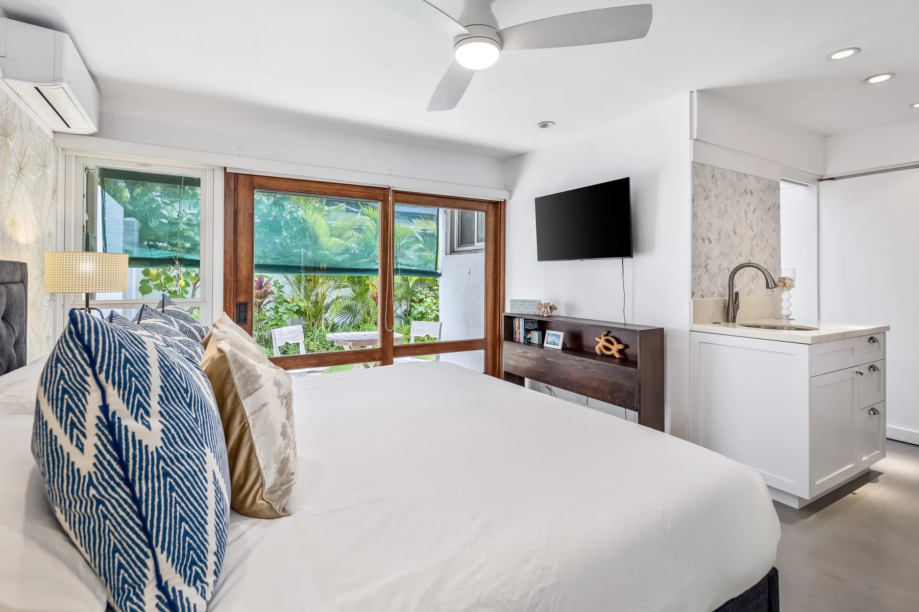 Un dormitorio con una cama junto a grandes ventanas y un televisor en la pared.