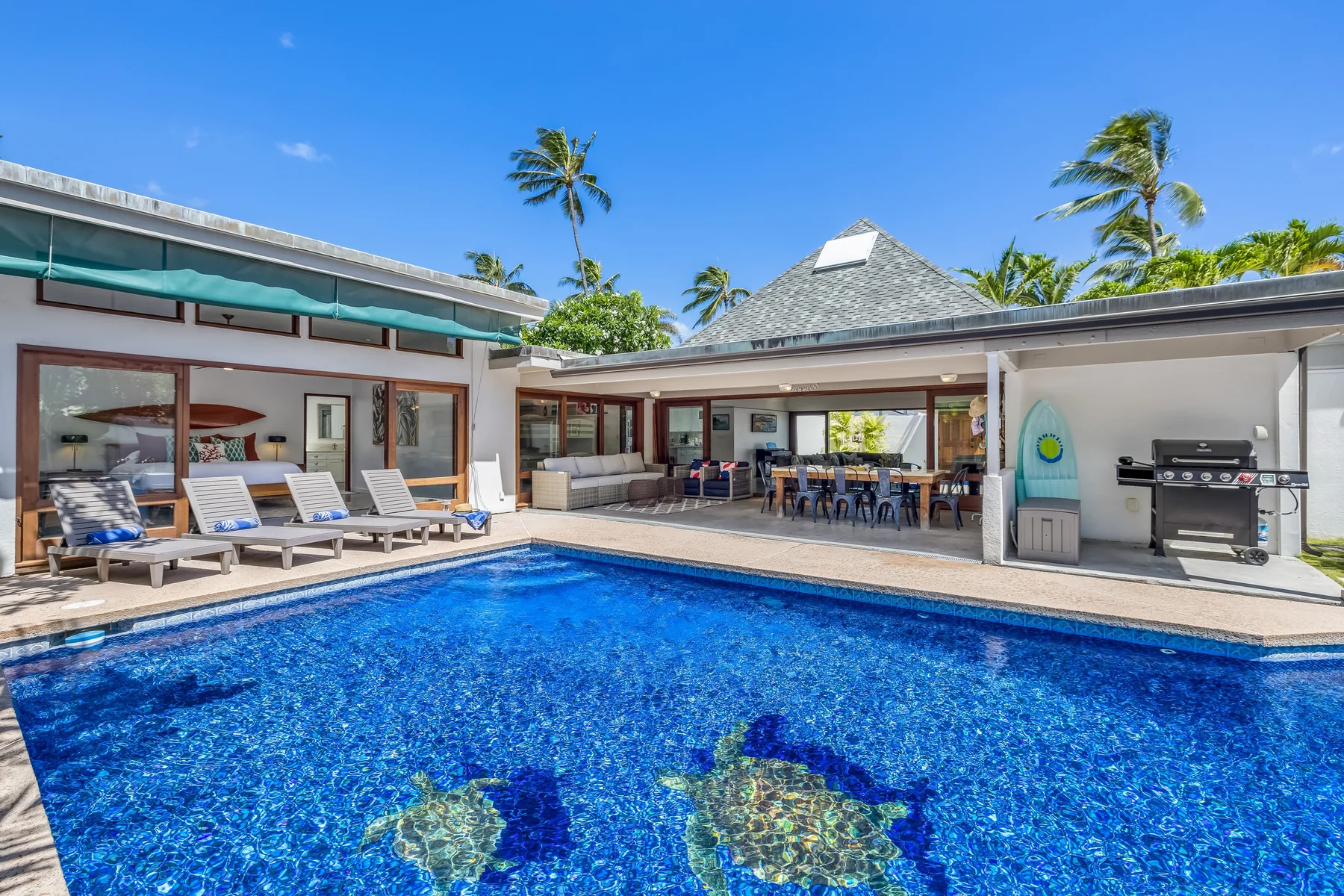 A tropical courtyard pool beside a covered outdoor dining area and lounge seating.