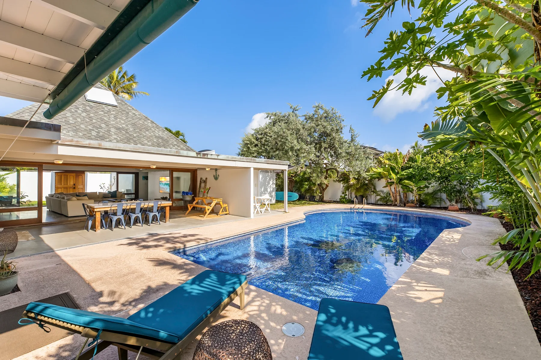 Una piscina junto a un patio con asientos al aire libre y un comedor cubierto.