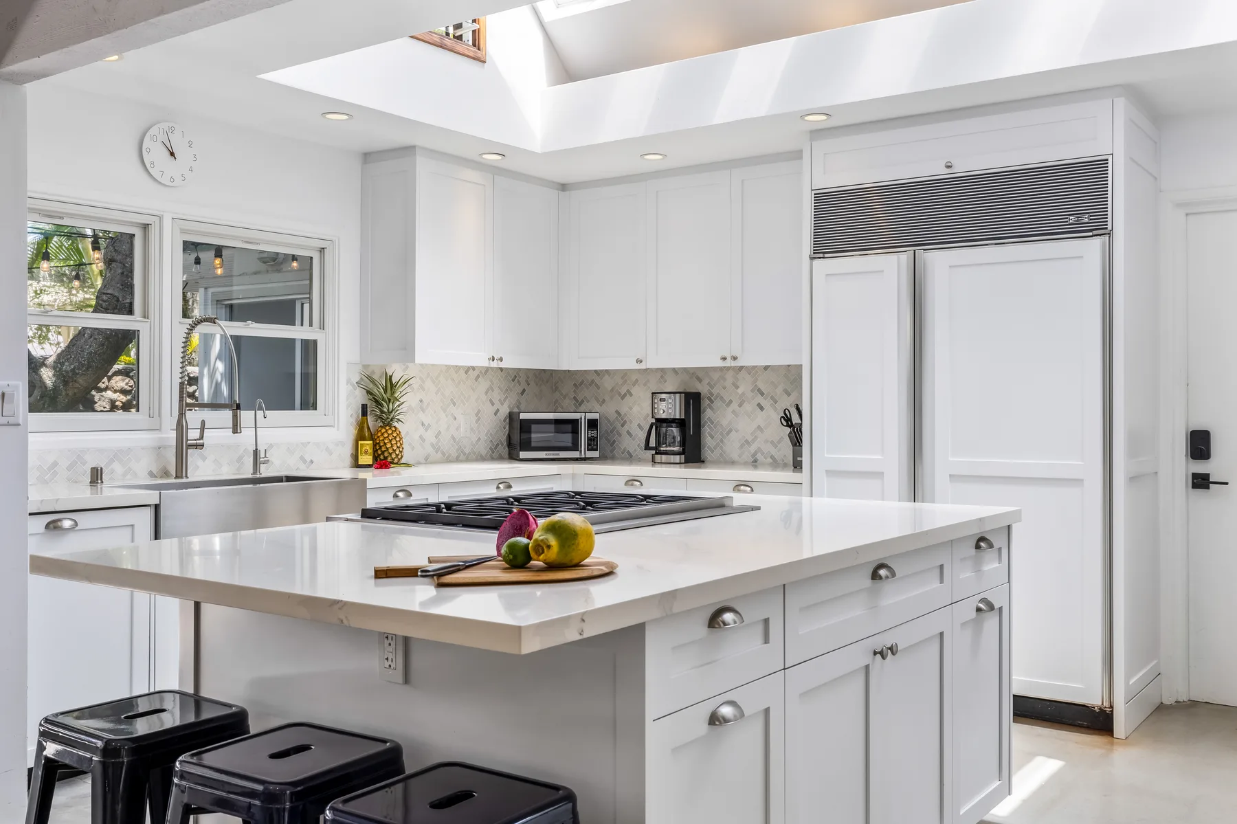 Una cocina blanca y luminosa con una isla grande y electrodomésticos sobre la encimera.