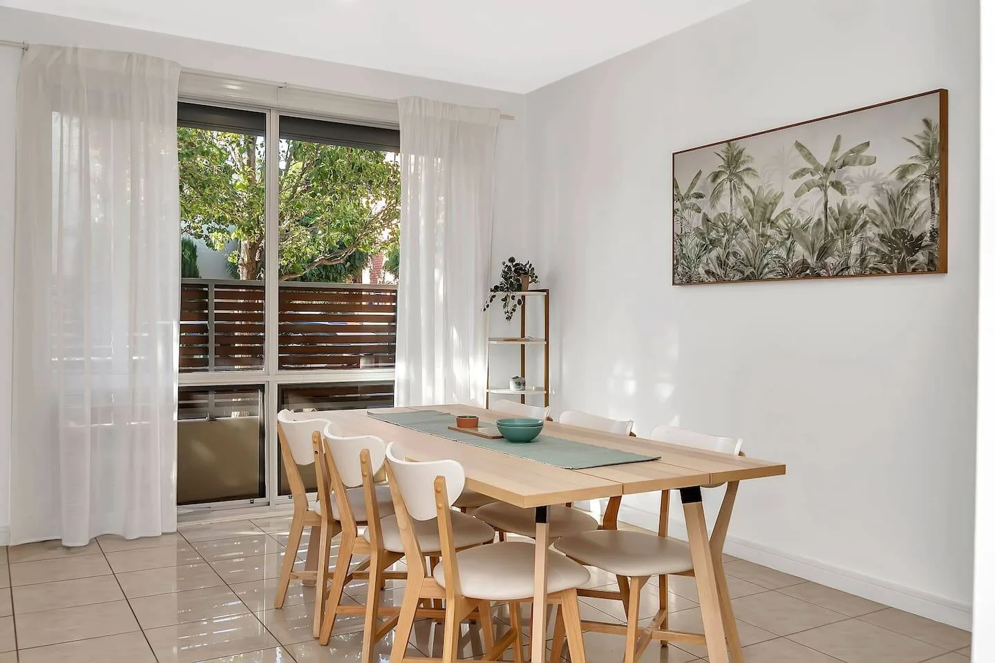 Un comedor luminoso con una mesa de madera, sillas y una lámina botánica enmarcada.