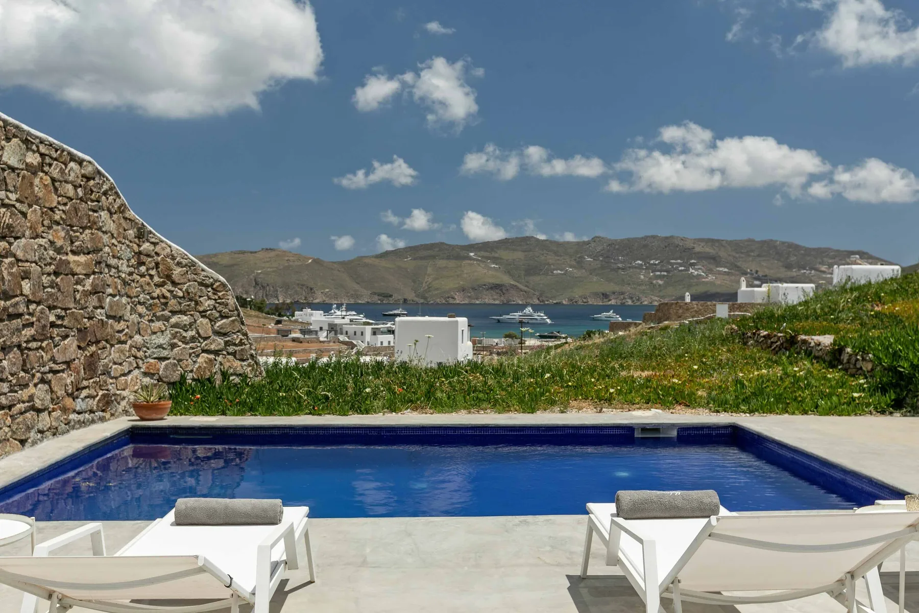 Una piscina exterior da a una bahía costera, con asientos de descanso en el patio.