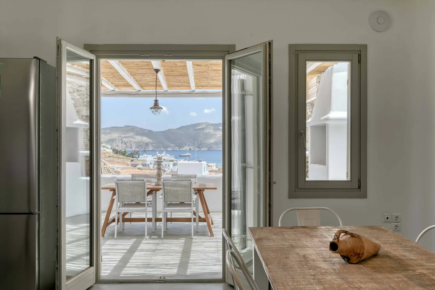 Una puerta abierta da a una zona de comedor junto al mar y montañas a lo lejos.