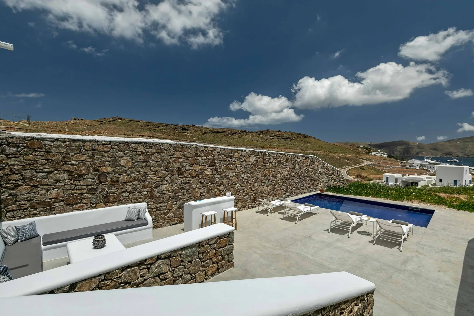 Una terraza exterior con piscina y asientos junto a un muro de piedra.