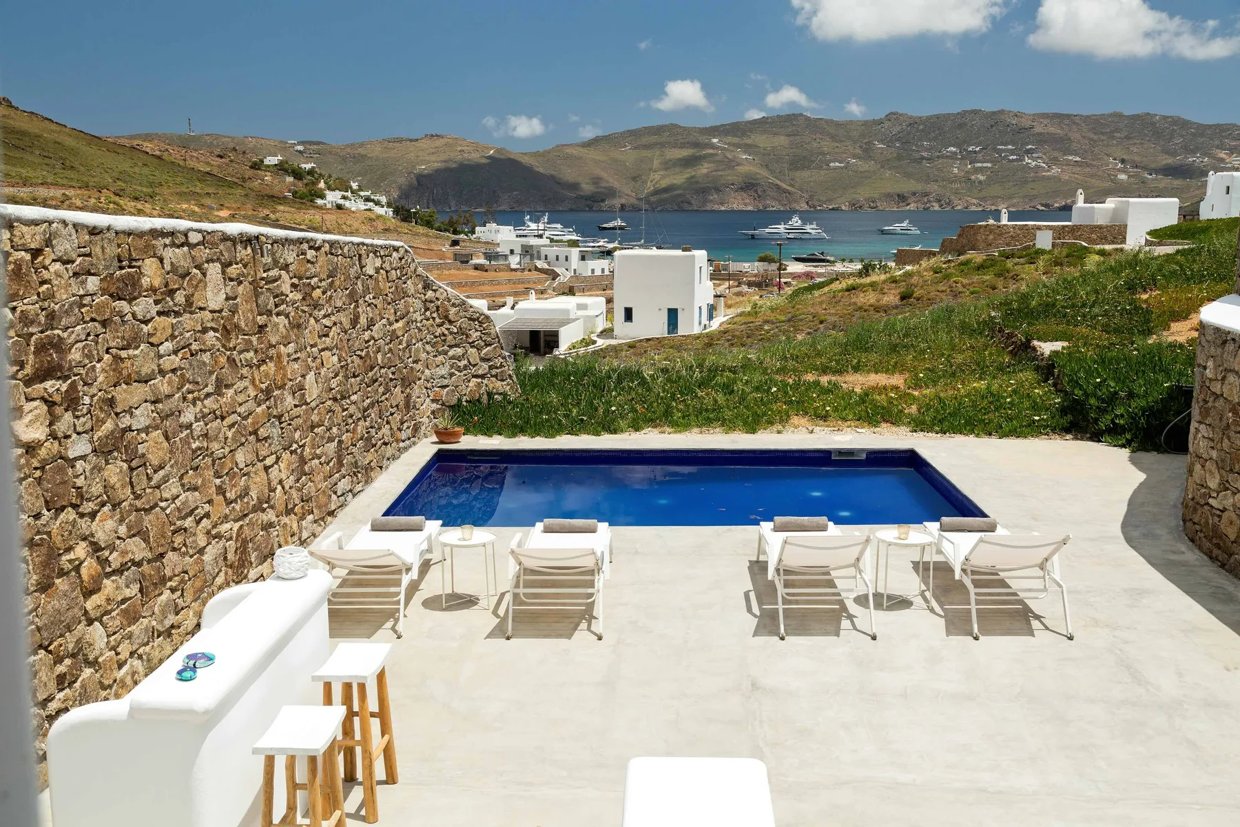 Terraza con piscina y asientos al aire libre, con vistas a una bahía y colinas.