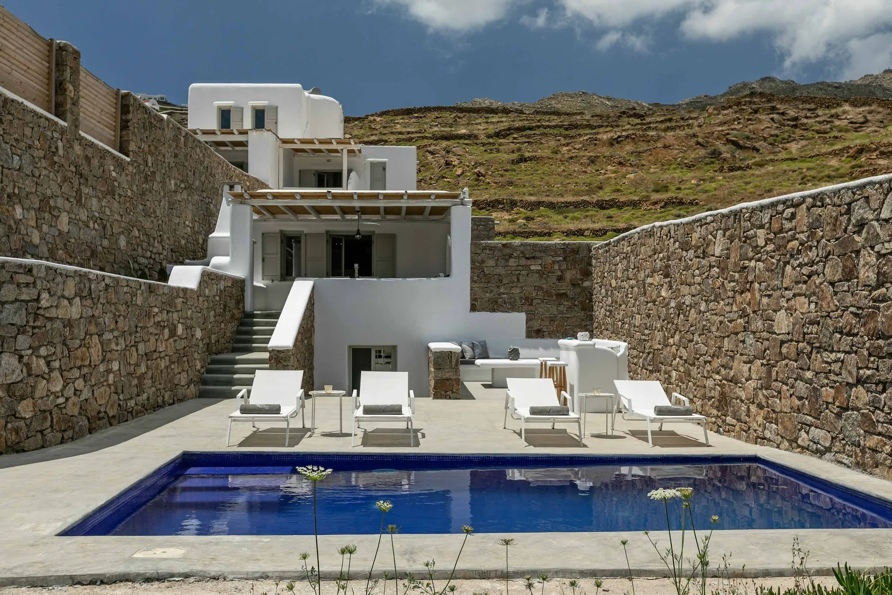 Una piscina azul está frente a una villa blanca entre muros de piedra.