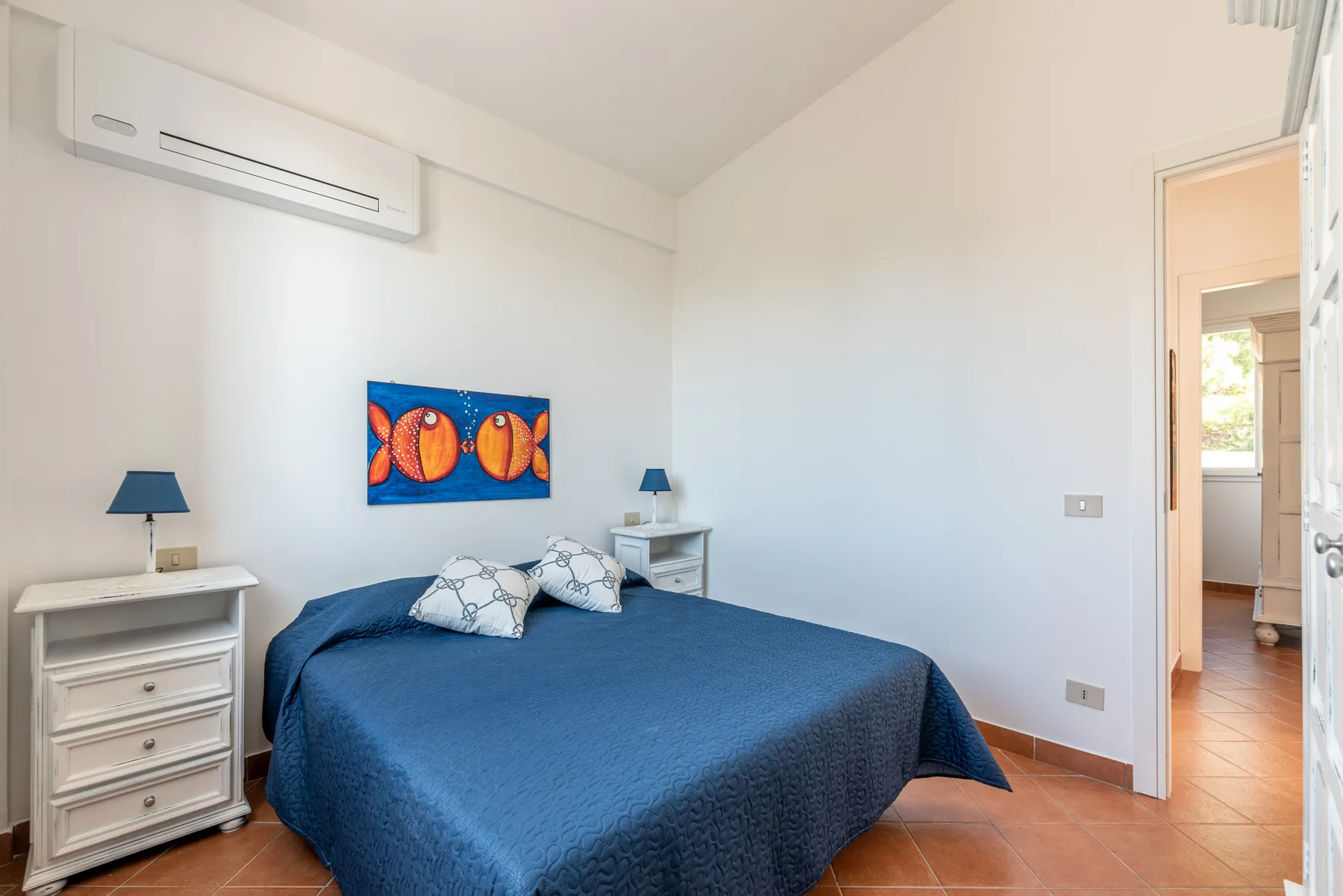A bedroom with a blue-covered bed and colorful fish artwork on the wall.