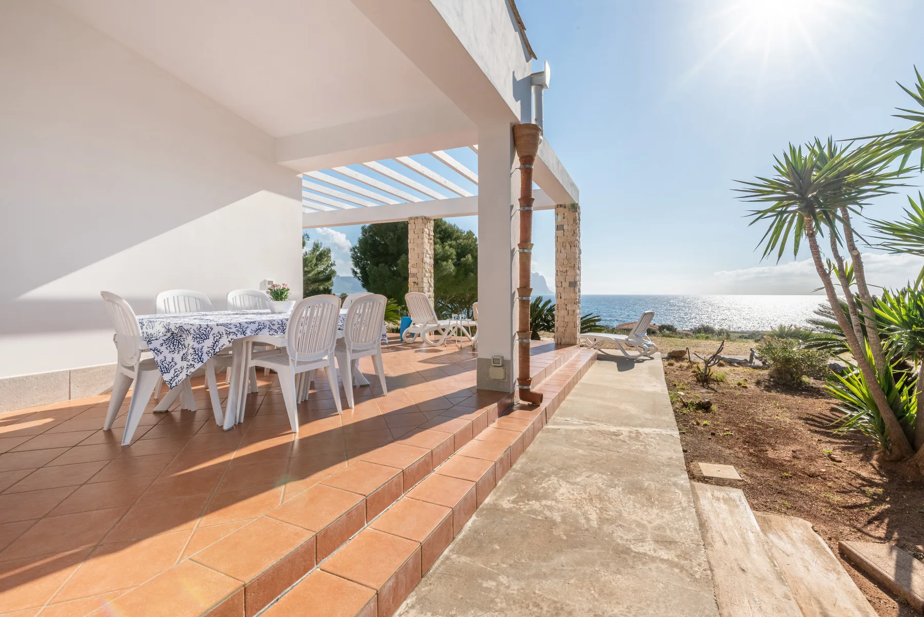A covered outdoor dining area opens onto a sunny coastal view.