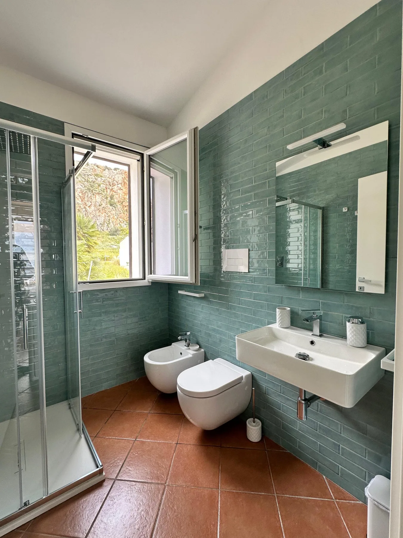 Un baño con paredes de azulejos verdes, ducha, inodoro y lavabo.