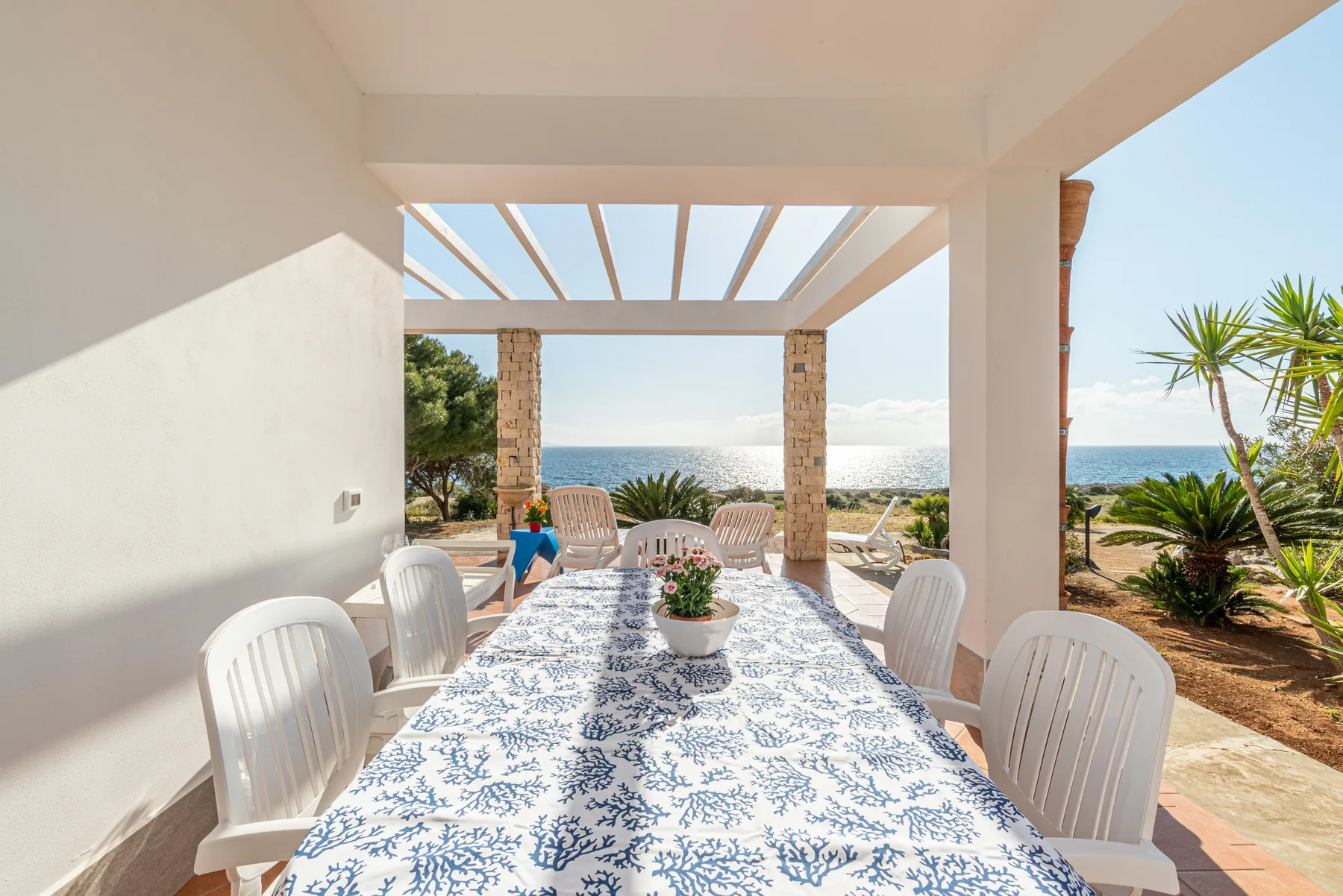 A covered outdoor dining area overlooks the sea, with a table set for a meal.